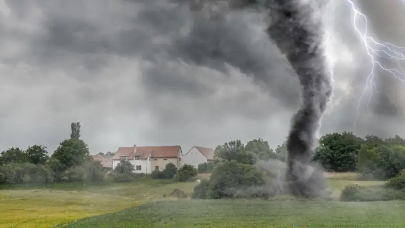 Black tornado funnel cloud and lightning touching down over an open field during a thunderstorm