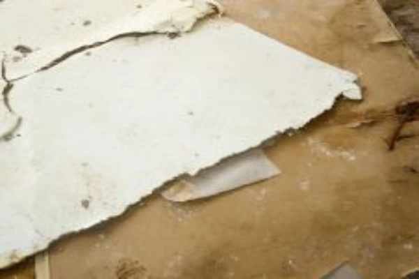 A close-up of a broken sheet of white plaster or drywall lying on top of a brown, dusty surface.