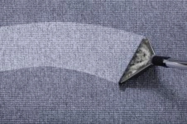 A close-up of a fabric surface being cleaned, with a metal tool removing dirt in a curved motion.